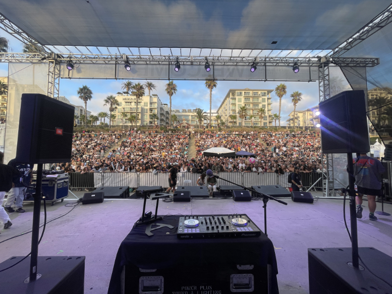 View from behind the DJ booth on the Power Plus Productions main stage at the 2024 Nissan Super Girl Surf Pro in Oceanside, CA, with a large crowd filling the amphitheater.
